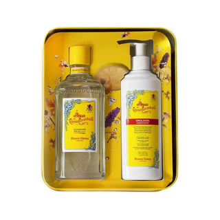 Conjunto de produtos ‘Agua de Colonia Concentrada’ da Álvarez Gómez, incluindo uma garrafa de colônia e uma garrafa de emulsão, exibidos em uma bandeja amarela com pétalas de flores espalhadas.